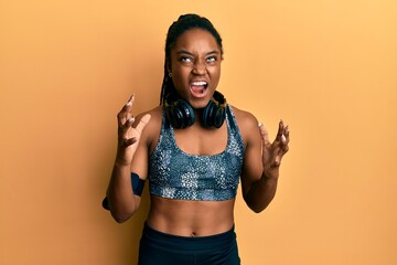 Poster - African american woman with braided hair wearing sportswear and arm band crazy and mad shouting and yelling with aggressive expression and arms raised. frustration concept.