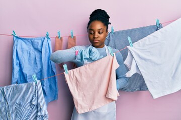 Wall Mural - African american woman with braided hair washing clothes at clothesline checking the time on wrist watch, relaxed and confident