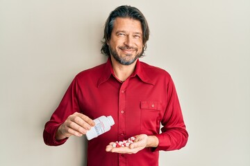 Poster - Middle age handsome man taking pills smiling with a happy and cool smile on face. showing teeth.