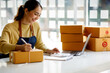 © David - Startup SME small business entrepreneur SME of freelance Asian woman using a laptop with box Cheerful success Asian woman her hand lifts up online marketing packaging box and delivery SME idea concept