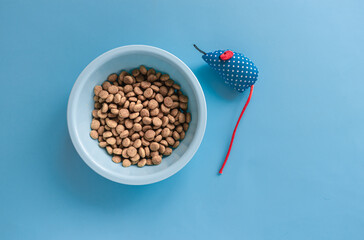 On a blue background there is a blue bowl with dry pet food next to toys. Layout for pets.