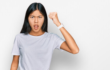 Poster - Beautiful young asian woman wearing casual white t shirt angry and mad raising fist frustrated and furious while shouting with anger. rage and aggressive concept.