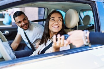 Young hispanic couple driving auto at the city. Girl smiling happy holding key of new car.