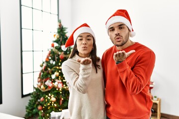 Canvas Print - Young hispanic couple standing by christmas tree looking at the camera blowing a kiss with hand on air being lovely and sexy. love expression.