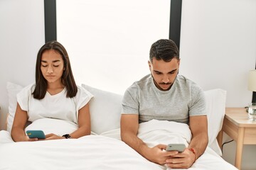 Sticker - Young latin couple using smartphone lying on bed at home.