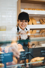 Wall Mural - Beautiful young and happy female worker working in a modern bakery or fast food restaurant.