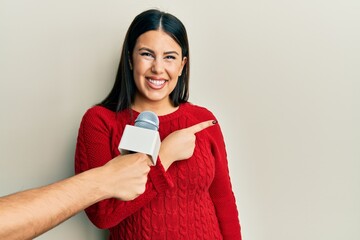 Canvas Print - Beautiful brunette woman being interviewed by reporter holding microphone smiling cheerful pointing with hand and finger up to the side