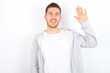 young caucasian man wearing casual clothes over white background waiving saying hello or goodbye happy and smiling, friendly welcome gesture.
