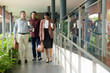 © DragonImages - Cheerful business colleagues drinking take out coffee when walking to meeting room in office