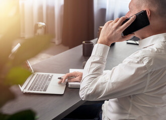 Poster - Businessman talking on mobile phone while looking at laptop screen. Business call in office.