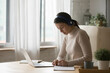 © fizkes - Diligent woman student studying from home, wear headphones use laptop, write notes, make assignment in copybook, listen audio course, improve foreign language knowledge use tech. Webinar event concept