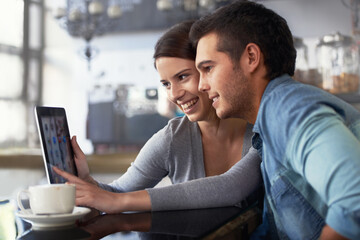 Poster - Showing him her online photo album. Shot of a young couple looking at a digital tablet while sitting in a cafe.