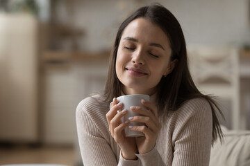 Close up beautiful woman relaxing on sofa with eyes closed, hold tea cup, take break at home enjoy favourite beverage looks carefree, relish aroma of coffee, daydreams alone indoor. No stress concept