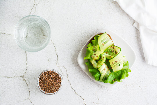 Fresh sandwich on rye bread with lettuce, cucumber and flax seeds on a plate and a glass of water on the table. Diet vegetarian food. Eco-friendly lifestyle. Top view.