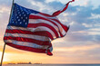 Broken U.S. flag in motion at sunset with ships at sea in the background.