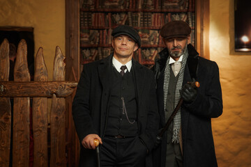 Two men of different ages, English retro gangster of the 1920s dressed in a coat, suit and flat cap in Peaky blinders style.