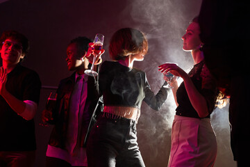 Wall Mural - Backlit portrait of two young women dancing in crowd while partying in smoky club, copy space