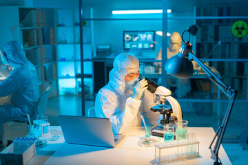Aufkleber - Female scientist in biohazard suit, respirator and gloves using microscope for studying new substances and their characteristics