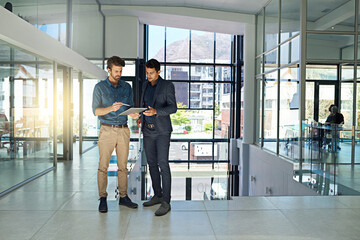Aufkleber - They collaborate on all the big projects. Shot of two colleagues talking together over a digital tablet while standing in a modern office.