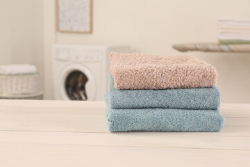 Poster - Stack of clean terry towels on white wooden table in laundry room