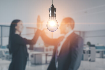 Canvas Print - Blurry businessman and woman working together on abstract office interior background with glowing light bulb. Work ideas and innovations concept. Mock up place for your advertisement.