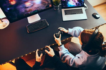 Wall Mural - Friends playing video game at home. Gamers holding gamepads sitting at front of screen. Streamers girl and boy playing online in dark room lit by neon lights. Competition and having fun