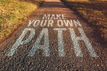 Make your own path motivational quote on footpath leading through park in diminishing perspective