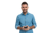 Fototapeta Na ścianę - happy unshaved man in denim shirt smiling while holding mobile