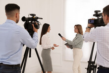 Professional Journalist Interviewing Young Business Woman And Cameramen Shooting Video For Broadcast