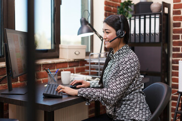Wall Mural - Call center smiling employee wearing headset answering voicecall regarding customer complaint. Confident asian customer support operator on call with client talking about project financial risks.