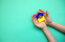 A House Cut Out Of Paper Painted In The Colors Of The Ukrainian Flag In The Hands Of A Child. The Child Is Holding A Paper House. Ukrainian Flag. There Is A Copyspace
