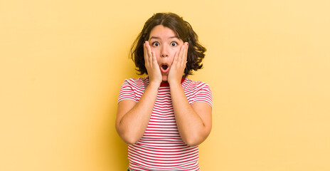 Wall Mural - pretty hispanic woman feeling shocked and scared, looking terrified with open mouth and hands on cheeks