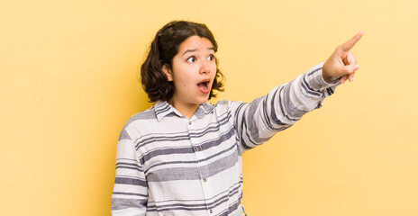 Wall Mural - pretty hispanic woman feeling shocked and surprised, pointing and looking upwards in awe with amazed, open-mouthed look