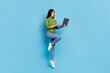 Full body photo of funky millennial brunette lady jump with laptop wear jumper jeans sneakers isolated on blue background