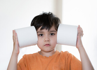 Portrait young boy with looking out and playing with toilet paper, Kid putting  toilet roll on his head, Child holding two white tissue, Children health care concept