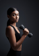 Poster - Two of the most intimidating traits are strength and beauty. Studio portrait of a young sportswoman doing dumbbell exercises against a gray background.