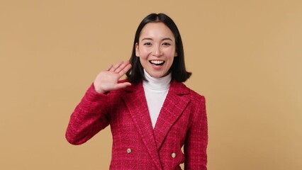 Wall Mural - Happy excited young woman of Asian ethnicity 20s wears red jacket look around for friend find waving meet greet with hand as notices someone isolated on plain pastel beige background studio portrait