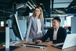 © Liubomir - Female boss flirts with male employee, businesswoman sitting at desk and smiling then Asian
