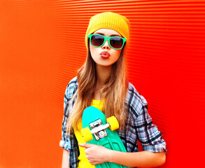 Poster - Portrait of stylish blonde young woman model with skateboard wearing colorful yellow hat on red background