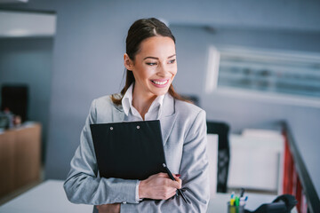 Wall Mural - Portrait of happy businesswoman holding clipboard at office.