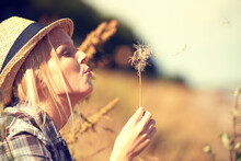 Blowing Away Her Cares.... Beautiful Young Woman Wearing A Straw Fedora And Blowing At A Dandelion.