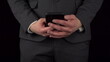 A young businessman in a suit takes out a phone from his pocket and texts in it. The waist of a man close-up on a black background.