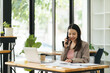 © PaeGAG - Asian businesswoman talking on the phone using laptop at the office.