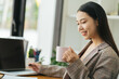 © PaeGAG - Benefits of remote work. Dreamy lady enjoying coffee during work on laptop computer in city cafe, smiling and looking aside. Young freelancer having break while working online in internet