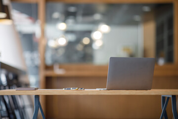 Wall Mural - Laptop Computer, notebook, and eyeglasses sitting on a desk in a large open plan office space after working hours