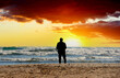 © MaxSafaniuk - Man at beach near sea on sunset. Back side of European man 40-70s in jacket, standing and waiting or thinking about something, in feeling lonely sadness. Male at beach during storm with waves in sea.