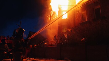 The roof of the house is on fire. The residential building burn, village. Firefighters put out a fire from the crane from above. The fire Department putting out the open flame. Smoke and sparks.