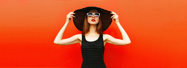 portrait of beautiful young woman wearing a black summer hat and dress on red background