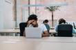 © EFStock - Unhappy Black man sitting at table touching forehead during work in office. Burnout at work fatigued from computer headache