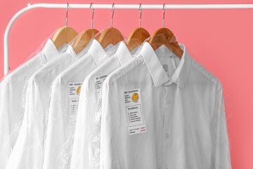 Poster - Rack with clean white shirts in plastic bags on pink background, closeup